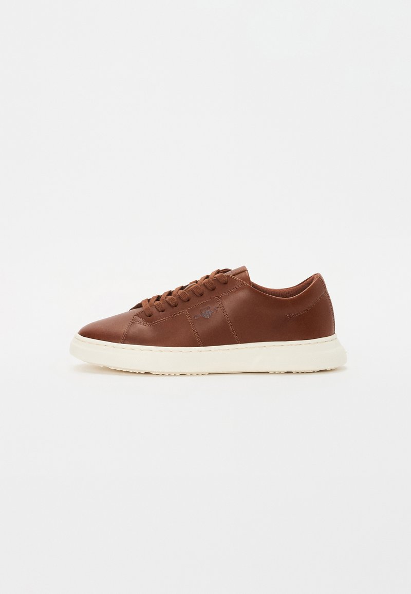 Braune Ledersneaker mit einer weißen Gummisohle, ausgestattet mit Schnürsenkeln und einem einfachen, glatten Design. Dezente, geprägte Logodetails an der Seite.