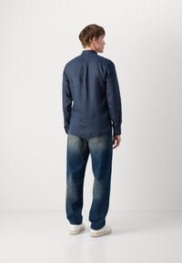 Navy blue long-sleeve button-up shirt with a straight cut, paired with light blue baggy jeans and white sneakers.