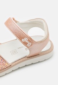 Rosa und goldene Sandalen mit einem glitzernden Riemen, verstellbarem Klettverschluss, gepolsterter Innensohle und strukturiertem Gummi sohle für besseren Halt.