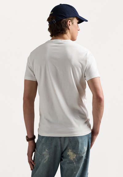 Tricou alb cu mânecă scurtă, din bumbac, cu gât rotund, purtat împreună cu blugi de culoare albastru deschis, cu detalii uzate și buzunare.