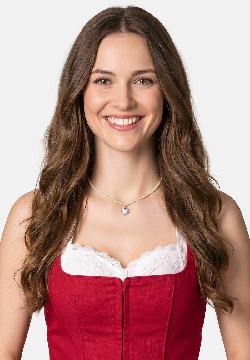 Young woman with long brown hair smiles, wearing a red dress with white lace and a pearl necklace with a heart pendant.