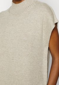 Top en tricot beige avec col montant, manches courtes et finition texturée. Doté d'une coupe décontractée et d'évasements sur les côtés pour une meilleure liberté de mouvement.