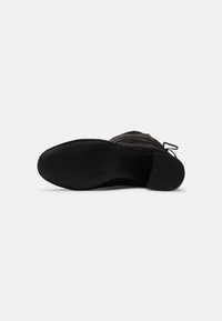 Suela de zapato negra que presenta una superficie de goma texturizada, con un tacón bajo y bordes suaves, diseñada para ofrecer tracción y durabilidad.