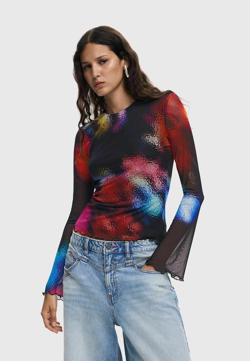 Bluză cu mânecă lungă dintr-un material negru transparent, având un model abstract colorat. Margină ondulată și manșete evazate. Se potrivește cu blugi de culoare bleu deschis.