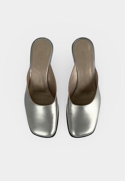 Paire de mules métalliques argentées à enfiler, avec bouts carrés et dos ouverts, vues de dessus sur un fond clair uni.