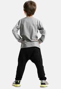 Graues Langarmshirt kombiniert mit schwarzen Hosen mit tiefer Schrittnaht. Die Schuhe haben graue, gelbe und schwarze Akzente. Das Kind steht mit den Händen in den Hüften.