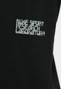 Μαύρο ύφασμα με λευκό κεντημένο κείμενο που αναγράφει «NIKE SPORT RESEARCH LABORATORY» σε στιλιζαρισμένη γραμματοσειρά μπλοκ.