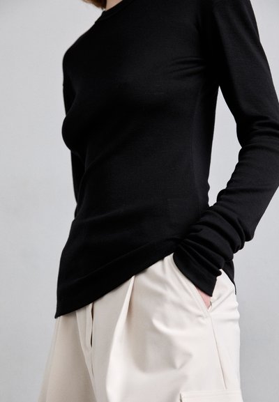 Top aderente nero a maniche lunghe realizzato in tessuto liscio, con scollatura rotonda e vestibilità rilassata in vita, abbinato a pantaloni plissettati color crema.