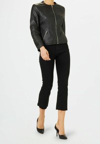 Veste en cuir noir à la coupe ajustée, fermeture éclair à l'avant et deux poches latérales. Associée à un pantalon noir raccourci et des chaussures à talons hauts noires.