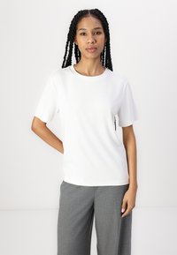 Vit kortärmad T-shirt med rund halsringning, tillverkad av ett slätt tyg. Bärs med ljusgrå skräddarsydda byxor, med en avslappnad passform.