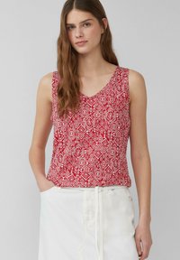 Top rosso senza maniche con un motivo geometrico bianco, scollatura a V, tessuto morbido e vestibilità rilassata, abbinato a una gonna bianca.