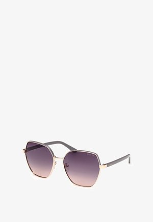 Gafas de sol hexagonales con lentes en degradado púrpura oscuro, acentos metálicos dorados y brazos de plástico gris con marca en un lado.