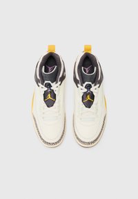 Hvide lædersneakers med sorte accenter, gule detaljer og en tekstureret grå mellemsål. Har en polstret krave og snøring.