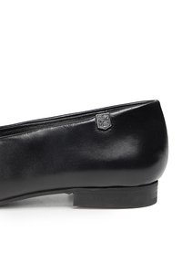 Zapato plano de cuero negro con un diseño elegante, textura suave, tacón bajo y un pequeño acento de logo metálico en el lateral.