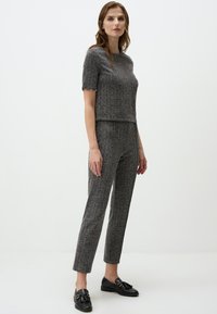Maglia grigia a maglia strutturata con maniche corte e polsini decorati, abbinata a pantaloni coordinati con una vestibilità slim e un motivo sottile. Scarpe nere.