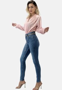 Blusa di satin rosa chiaro con maniche lunghe, abbinata a jeans di denim blu a vita alta con cintura a catena e sandali con tacco trasparente.