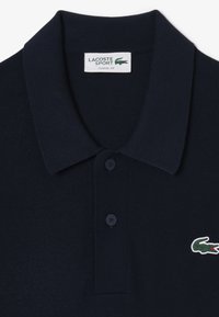 Marineblauwe polo met een klassieke pasvorm, voorzien van een geribbelde kraag, een placket met twee knopen en een groene krokodillologo op de linkerkant van de borst.