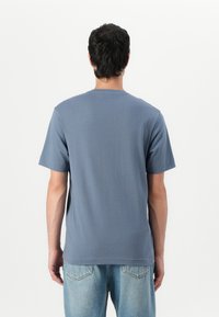 Kortermet t-skjorte i dempet blå farge, rund hals, glatt tekstur og enkelt design. Brukt sammen med lysblå denimjeans.