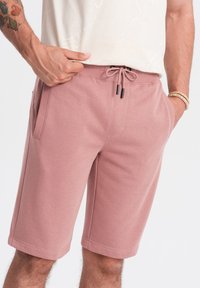 Svetle růžové šortky vyrobené z měkké tkaniny, s elastickým pasem s šňůrkou a bočními kapsami.