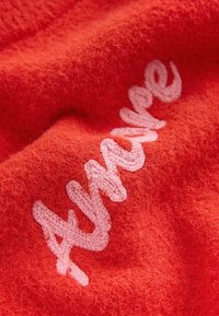 Tissu rouge texturé avec un texte tricoté rose épelant "Avenue" en style cursif.