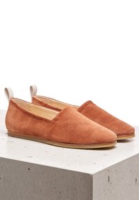 Zamszowe buty wsuwane w kolorze rdzawym, z ostrym noskiem i minimalistycznym designem, z beżową tkaniną przy pięcie oraz płaską skórzaną podeszwą.