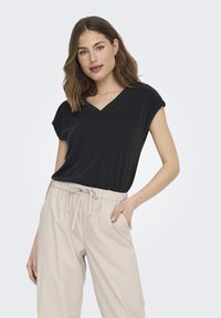 Haut noir à manches courtes en V, fabriqué dans un matériau doux, associé à un pantalon à taille élastique beige clair, avec des poches latérales.