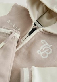 Jasno beżowa i mauve bluza z kapturem na zamek, z prążkowanymi mankietami, z nadrukiem logo i kontrastującymi białymi akcentami. Miękka tkanina z detalami faktury.