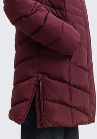 Bordeaux pufferjack met diagonale gestikte padding, zijritsen en een ademende stofstructuur. Lange mouwen met een slim-fit ontwerp voor de armen.