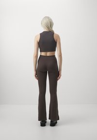 Brown crop top and flared pants made of ribbed fabric, featuring a high waistband and a smooth texture, with black footwear.