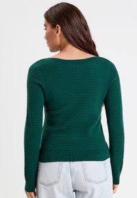Pull en maille texturée vert, à manches longues, avec une encolure large et des bords côtelés au niveau des poignets et de l'ourlet. Il présente un motif en nid d'abeille sur le tissu.