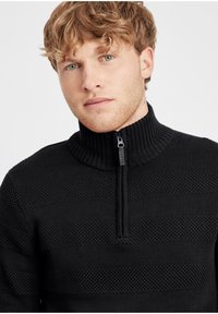 Pullover nero a maglia con colletto alto e mezza zip. Presenta strisce testurizzate e sezioni lisce, realizzato in tessuto morbido.