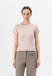 Light pink fitted t-shirt with short raglan sleeves, ribbed texture, round neckline. Paired with tailored beige trousers featuring front pocket.