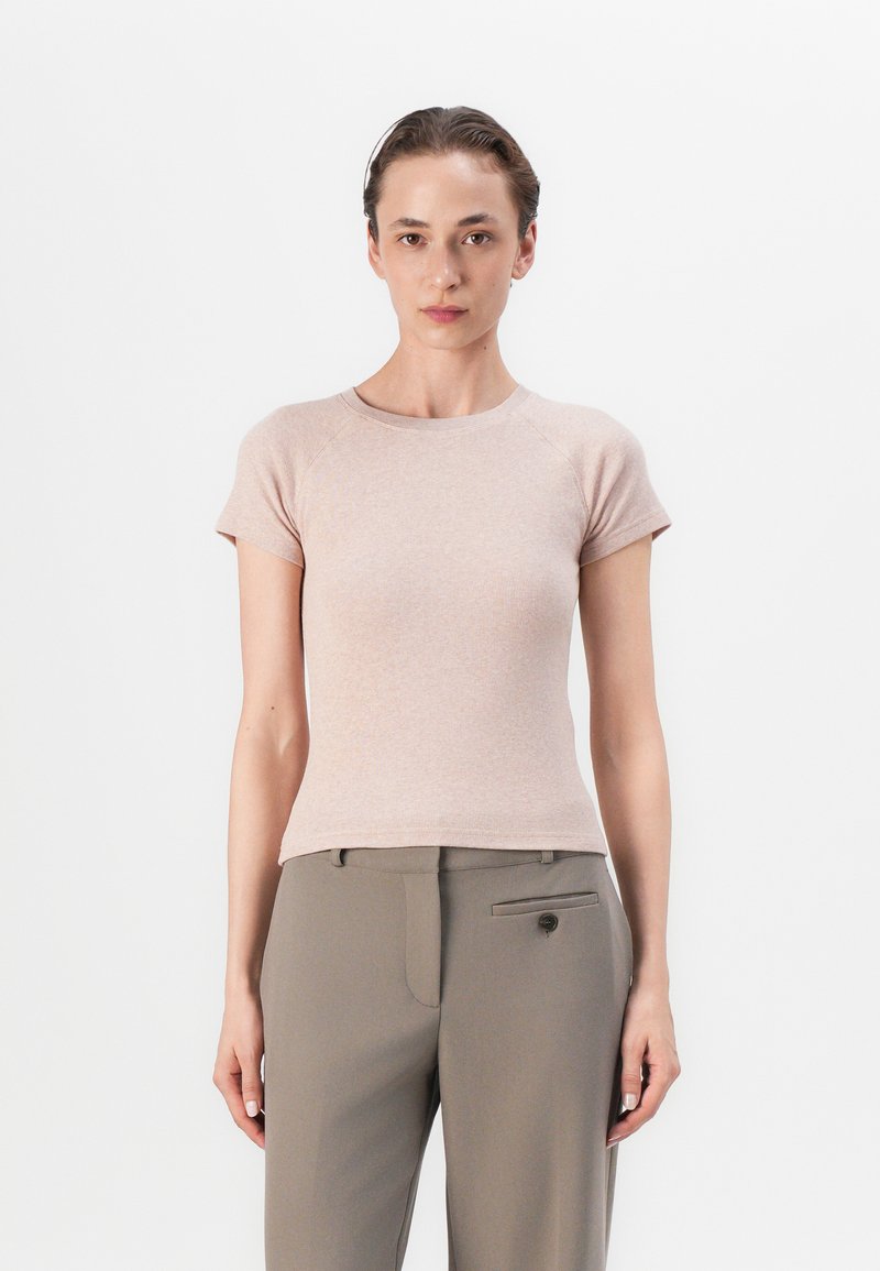 Light pink fitted t-shirt with short raglan sleeves, ribbed texture, round neckline. Paired with tailored beige trousers featuring front pocket.