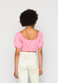 Blusa cropped rosa com mangas bufantes e um decote largo, combinada com calças de padrão xadrez gingham verde pálido. Tecido suave com detalhes franzidos.