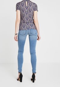 Korte ærmer med paisley-mønster i marineblå, parret med lyseblå skinny jeans. Sorte højhælede sko fuldender outfittet.