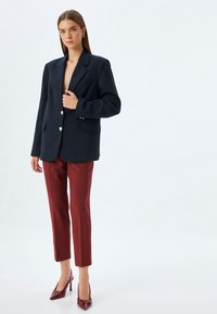 Navy blazer with a structured design, featuring two front pockets and silver buttons. Paired with maroon tailored trousers and glossy heels.