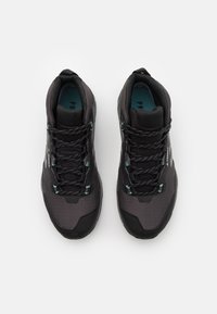 Schwarze Sportschuhe mit texturiertem Mesh-Obermaterial, türkisen Akzenten und schwarzen Schnürsenkeln. Dicke Gummisohlen bieten Stabilität und Unterstützung.