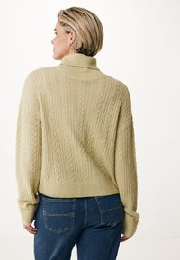 Maglione oversize a treccia in giallo chiaro, con colletto alto, polsini a coste e un motivo testurizzato; abbinato a jeans scuri.