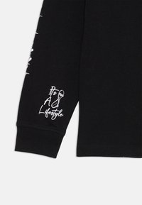 Schwarzes Langarmshirt mit weißem Text und Grafiken auf den Ärmeln. Der Baumwollstoff ist glatt, mit gerippten Bündchen und einem taillierten Schnitt.