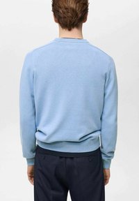 Pulover albastru deschis cu guler rotund și mâneci lungi, realizat dintr-un material tricotat texturat. Mansete și tiv cu model în relief. Purtați-l cu pantaloni închiși la culoare.