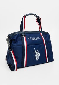 Borsa in nylon blu navy con dettagli a righe bianche e rosse, dotata di doppio manico, chiusura con zip e logo di un giocatore di polo in bianco.