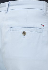 Φωτεινό γαλάζιο πίσω τσέπη παντελονιού με κούμπωμα και μικρό ορθογώνιο λογότυπο κόκκινο, άσπρο και ναυτικό πάνω από την τσέπη στη δεξιά πλευρά.