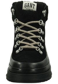 Schwarze Wanderschuhe mit einer strukturierten Oberseite, ausgestattet mit silberner Hardware und kontrastierenden beigen Schnürsenkeln. Dicke Gummisohle mit Profil.