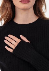 Pull noir côtelé avec un col rond et des manches allongées. Texture douce avec une coupe ajustée, mettant en valeur des lignes épurées sur le tissu.