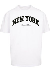 Balta medvilnės marškinėliai su dideliais juodais rašmenimis, kuriuose užrašyta "NEW YORK" virš "Upscale Studios" mažesniu šriftu.