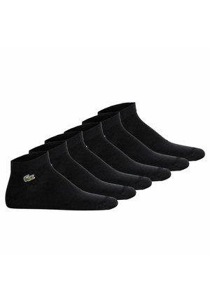 Chaussettes noires sœurs en rang, avec un côtelé au niveau de la cheville et un petit logo vert sur le côté. Fabriquées en tissu doux et texturé.