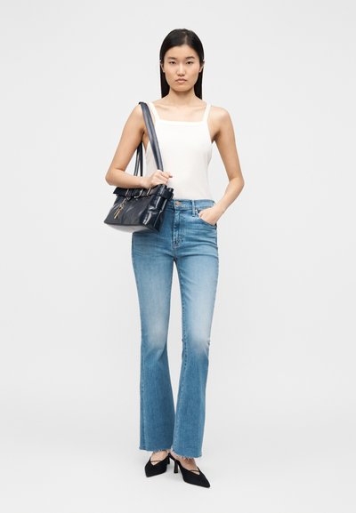 Fehér ujjatlan póló, világoskék bővülő farmernadrág és fekete magassarkú cipő. Fekete kézitáska strukturált kialakítással és cipzáras részlettel.