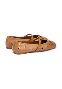 Ballet flats en cuir tan avec un bout arrondi, ornées de clous en argent décoratifs et d'un nœud à l'avant. Semelle plate.