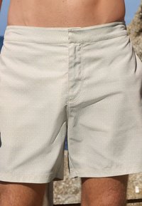 Swim shorts in light green with a wavy pattern, featuring an elastic waistband and side pockets, made from water-resistant fabric.