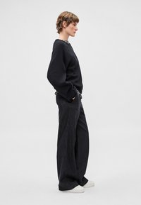 Melns džemperis ar brīvu piegriezumu, kopā ar tumšiem, plašiem biksēm. Apavi ir balti sporta apavi. Vienkāršs un minimālistisks dizains.